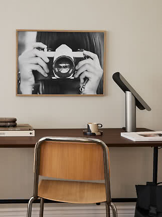 Scrivania con sedia in legno, lampada da tavolo e foto in bianco e nero incorniciata con fotocamera