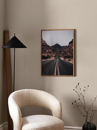 Indrammet plakat med ørkenvej mellem klipper hænger på beige væg i stue