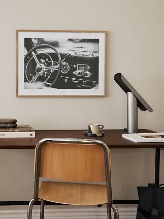 Skrivebord med stol, lampe og indrammet sort-hvid foto af et bilinteriør på væggen