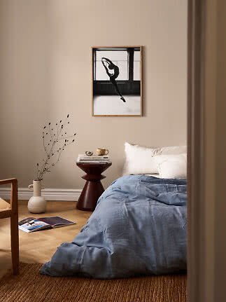 Affiche noir et blanc d’une danseuse encadrée au-dessus d’un lit dans une chambre beige