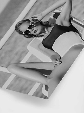 Black-and-white photo of woman in black swimsuit and white sunglasses on a lounge chair