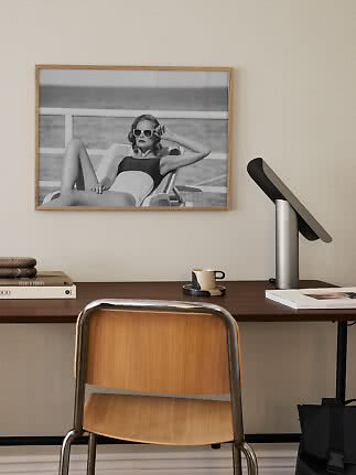 Home office with wooden desk, chair, table lamp and framed black-and-white photo on the wall