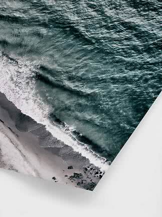 Canvas print with aerial view of waves crashing onto a dark sandy beach with rocks