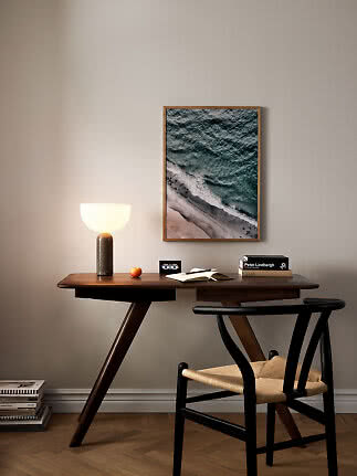 Dark wooden desk with glowing table lamp, chair, and framed ocean print on the wall
