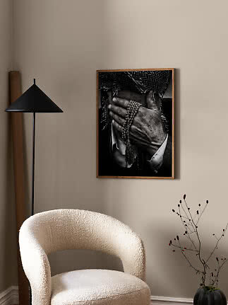 Indrammet sort-hvid foto af hænder med bedekæde på beige væg i moderne stue