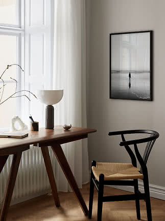 Minimalistisk hjemmekontor med træbord, sort stol og indrammet sort-hvid strandfoto på væggen