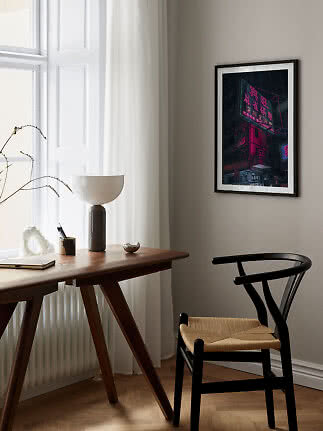 Gerahmtes Poster eines neonbeleuchteten Gebäudes über einem Schreibtisch im hellen Raum