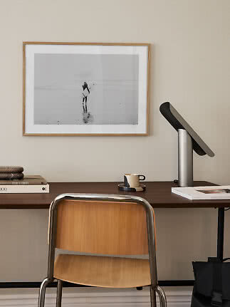 Donkerhouten bureau met stoel, lamp, kopje en ingelijste zwart-wit strandfoto aan de muur