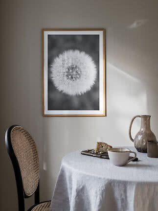 Affiche encadrée noir et blanc de pissenlit au mur au-dessus d’une table avec tasse et gâteau