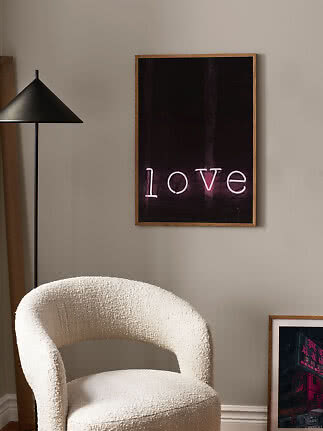 Framed poster with neon "love" sign on wall above a cream textured armchair