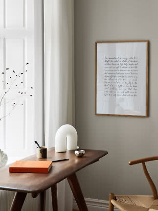 Indrammet plakat med håndskrift over et træbord i et lyst, minimalistisk rum