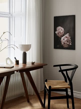 Skrivebordshjørne med sort stol, bordlampe og indrammet blomsterplakat på væggen