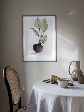 Gerahmtes Rote-Bete-Poster über einem Tisch mit Tasse, Krug und Kuchenstück.