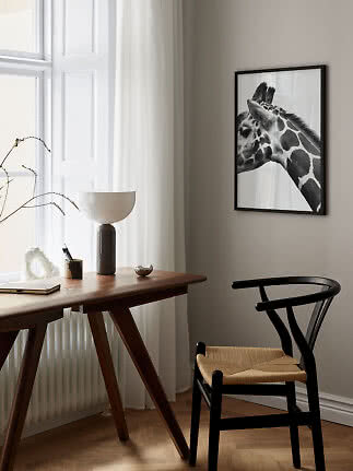 Sort-hvid girafplakat i sort ramme over et træskrivebord og sort stol ved et lyst vindue