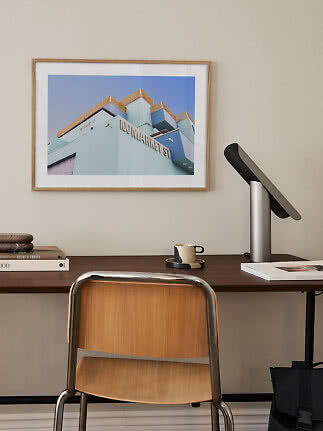 Framed photo of a blue building above a desk with lamp, cup and chair