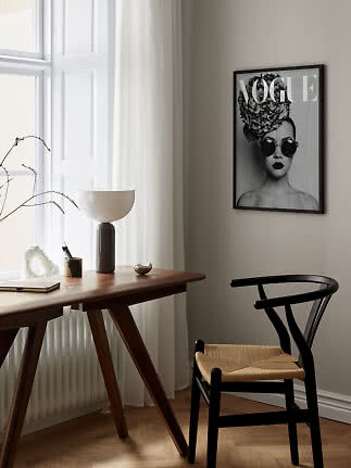 Black framed Vogue poster with woman in sunglasses above a desk in a bright room