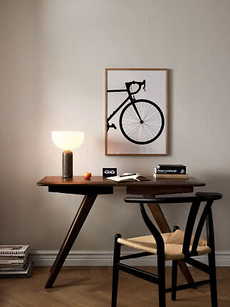 Dunkler Holzschreibtisch mit Tischlampe, Stuhl und Fahrradbild an beiger Wand.