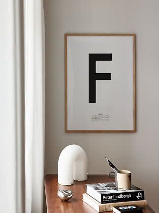 Inramad typografiaffisch med bokstaven F ovanför ett träbord med böcker, mugg och vit dekoration
