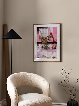 Lámina enmarcada de edificio rosa y plantas en pared beige sobre sillón claro