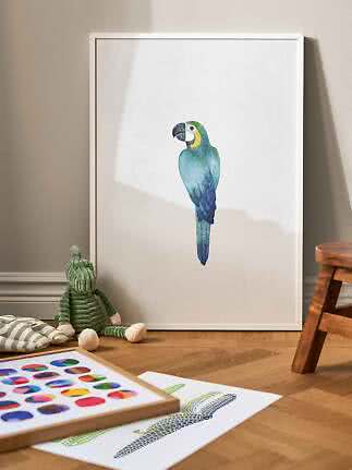 White framed poster with watercolor blue-green parrot, leaning against a wall on wooden floor.
