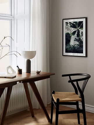 Indrammet botanisk plakat på væg over træskrivebord og sort stol ved et lyst vindue