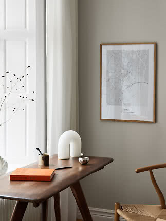 Gerahmter Tokio-Stadtplan über Holztisch mit Buch, Stift und weißer Lampe am Fenster