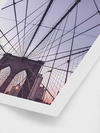 Fotografi af Brooklyn Bridge nedefra med kabler mod himlen i rosa aftenslys