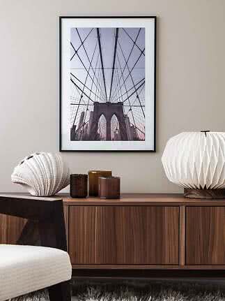 Indrammet foto af Brooklyn Bridge over et træskab med lampe, lysestager og muslingeskal