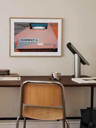 Gerahmter 'SUBWAY 4'-Print über einem Schreibtisch mit Lampe, Tasse und Holzstuhl
