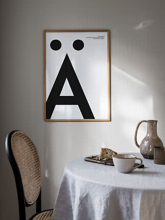Gerahmtes Typografie-Poster mit großem schwarzem Ä an heller Wand über Esstisch