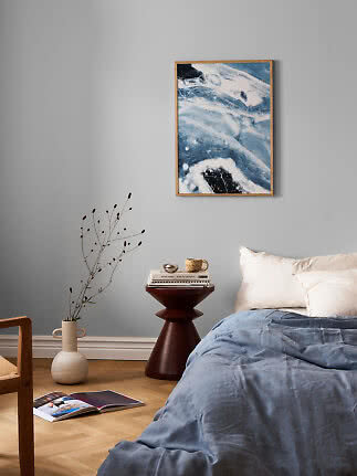 Schlafzimmer mit blauer Bettdecke, weißen Kissen und abstraktem blauen Wandbild