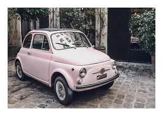 Light pink vintage car parked on a cobblestone courtyard in front of a leafy building