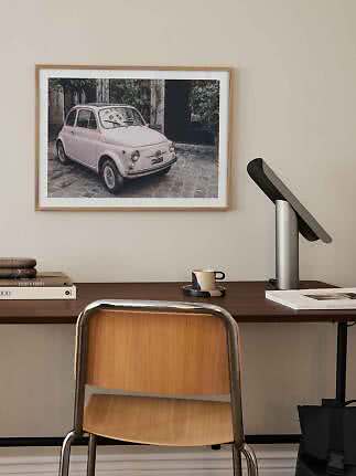 Framed print of a pink vintage car above a desk with lamp and chair