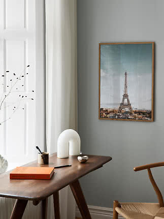 Gerahmtes Eiffel­turm-Poster an grauer Wand über einem Holztisch im hellen Raum