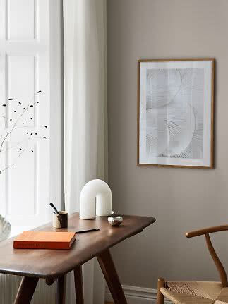 Gerahmter abstrakter Print über dunklem Holztisch am Fenster in hellem, minimalistischem Raum
