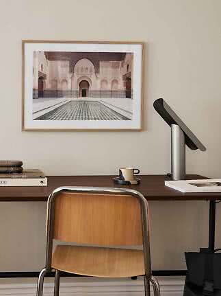 Desk with wooden chair, table lamp, and framed courtyard print on a beige wall