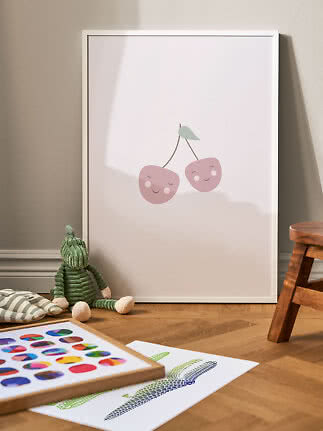 Póster infantil con marco blanco y dos cerezas rosas sonrientes, apoyado en la pared