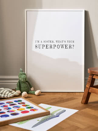 White framed poster with the quote "I'm a sister, what's your superpower?" on a nursery floor.