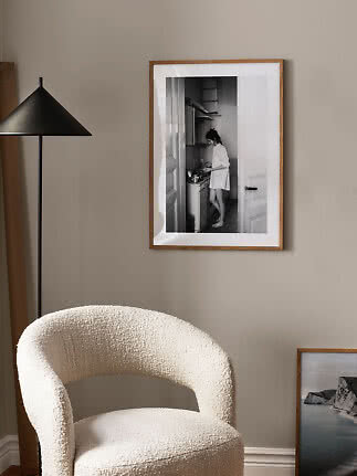 Indrammet sort-hvid foto på beige væg over en cremefarvet lænestol ved en sort gulvlampe