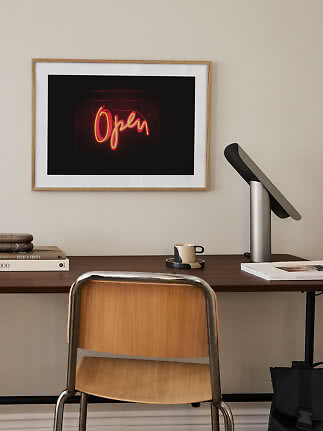 Lámina enmarcada con letrero de neón rojo "Open" sobre un escritorio
