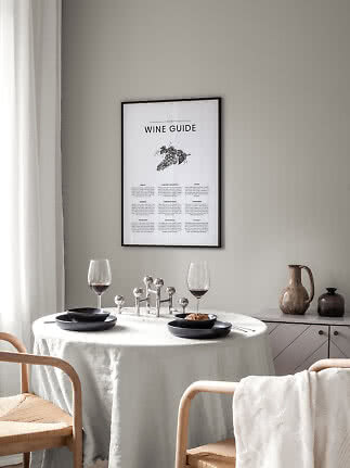 Indrammet vinplakat over et dækket spisebord med to vinglas og sorte tallerkener