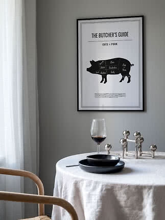 Gerahmtes schwarz-weiß Poster mit Schweinefleisch-Zuschnitten über gedecktem Tisch an grauer Wand