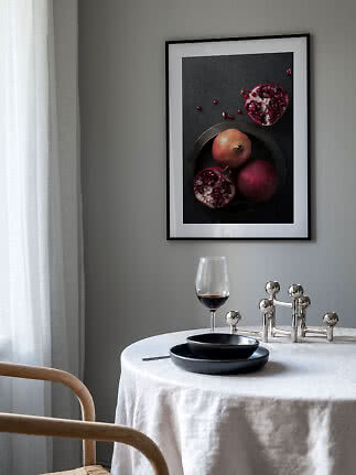 Table à manger avec vaisselle noire, verre à vin et affiche encadrée de grenades sur mur gris