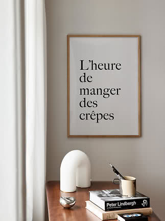 Poster incorniciato con testo francese su parete beige sopra tavolo in legno con libri e tazza