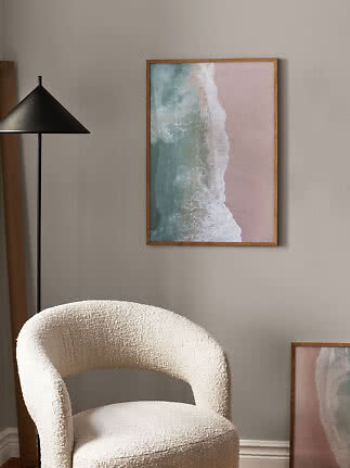 Framed beach print with waves on pink sand hanging above a cream textured chair