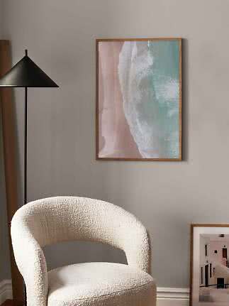 Framed beach wave print on wall above a cream boucle chair beside a black floor lamp