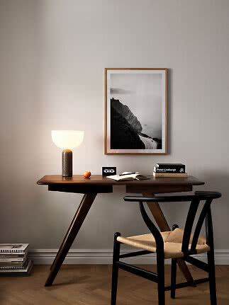 Dark wooden desk with chair, lit table lamp and framed black-and-white landscape photo
