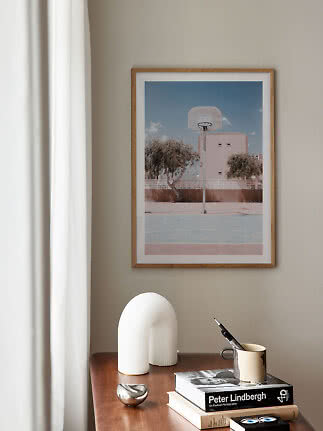 Framed basketball court print above a wooden table with books and decorative objects
