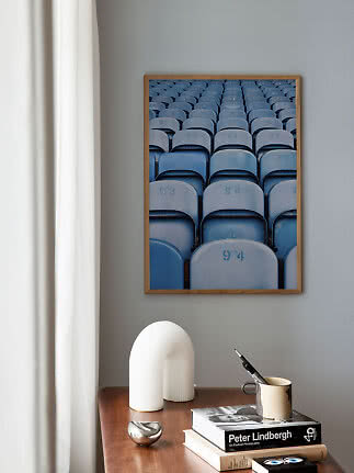 Gerahmtes Poster mit Reihen blauer Stadionsitze an grauer Wand über einem Holztisch
