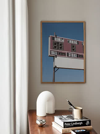 Gerahmter Print einer Baseball-Anzeigetafel über einem Holztisch mit Büchern und Deko